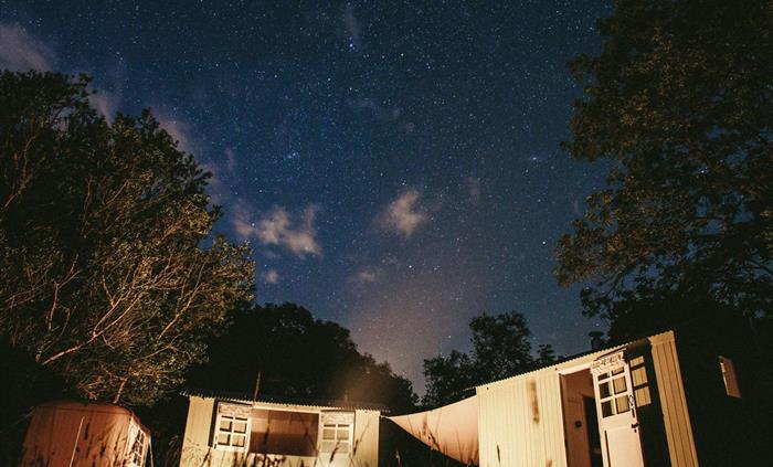 The shepherds' huts are lit up by the firepit in the foreground with the starry skies of Snowdonia Dark Sky Reserve overhead